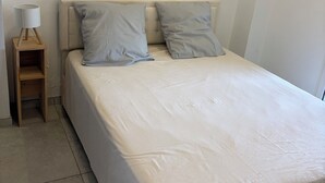 A bedroom with a bed, two pillows, a nightstand, and a lamp. - Vrbo Property (Sausset-les-Pins)