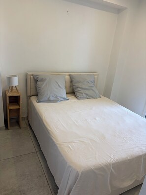 Een slaapkamer met een bed, twee kussens, een nachtkastje en een lamp.