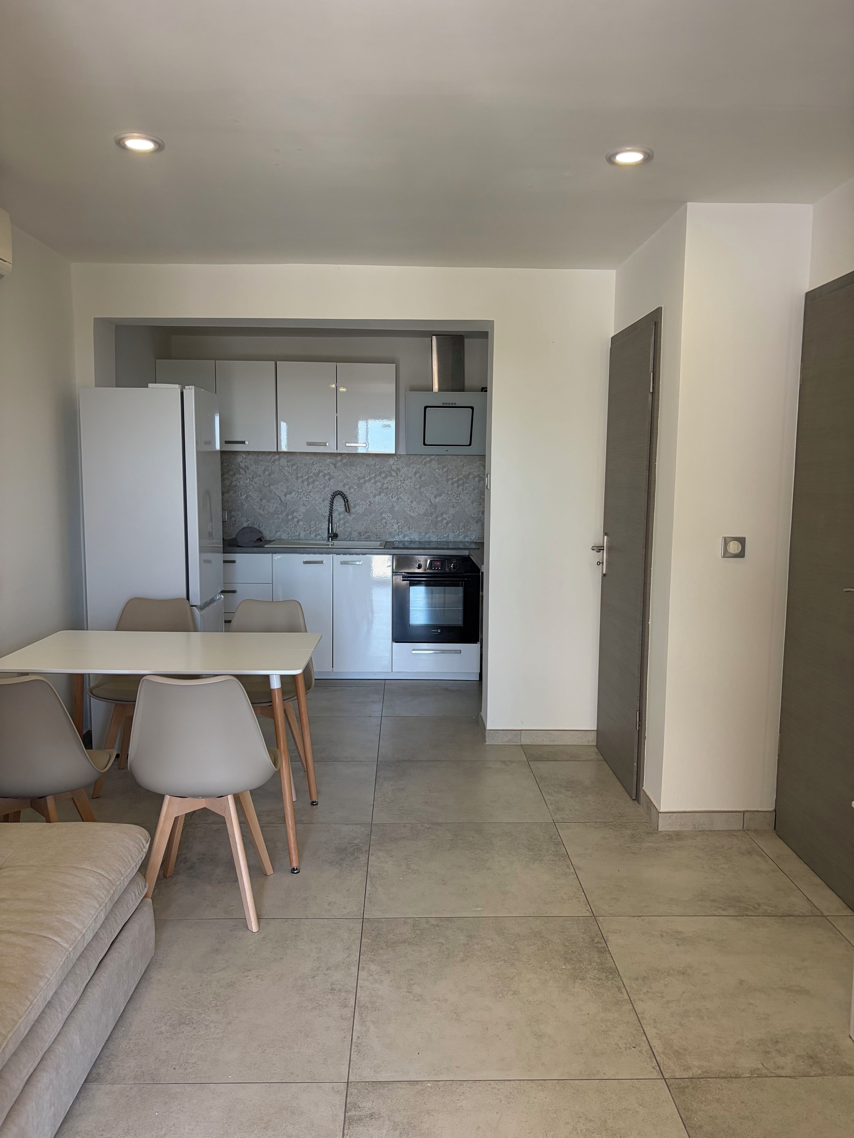 Una cucina moderna con mobili bianchi, forno a incasso e zona pranzo con tavolo e sedie.