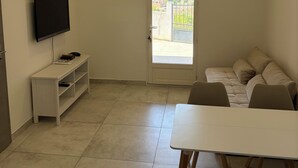 A room with a television on a stand, a sofa, a dining table, and a door leading to an outdoor area. - Vrbo Property (Sausset-les-Pins)