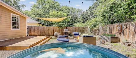 A backyard with a swimming pool, wooden deck, outdoor furniture, and a hammock.