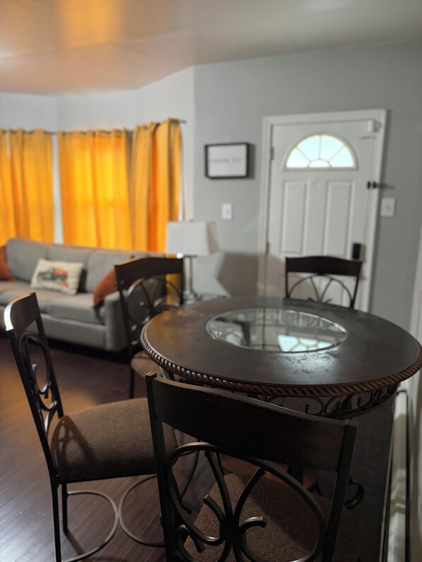 A dining area with a round table and chairs, a sofa, and curtains in the background.