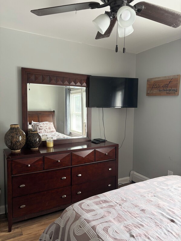 A bedroom with a wooden dresser, a flat-screen TV, a ceiling fan, and a bed with patterned bedding. - Modern, Two Family Home in Orange (City of Orange)