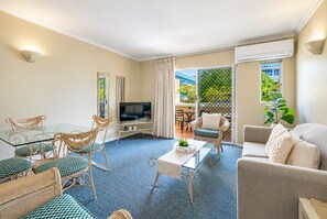A living room with a glass coffee table, wicker chairs, a sofa, and a television. - Heart of Cairns- Boutique apartment, Balcony & Pool (Cairns City)