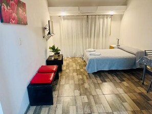 Ein kleines Zimmer mit Bett, einem Tisch, einer Sitzbank und einem an der Wand befestigten Fernseher.