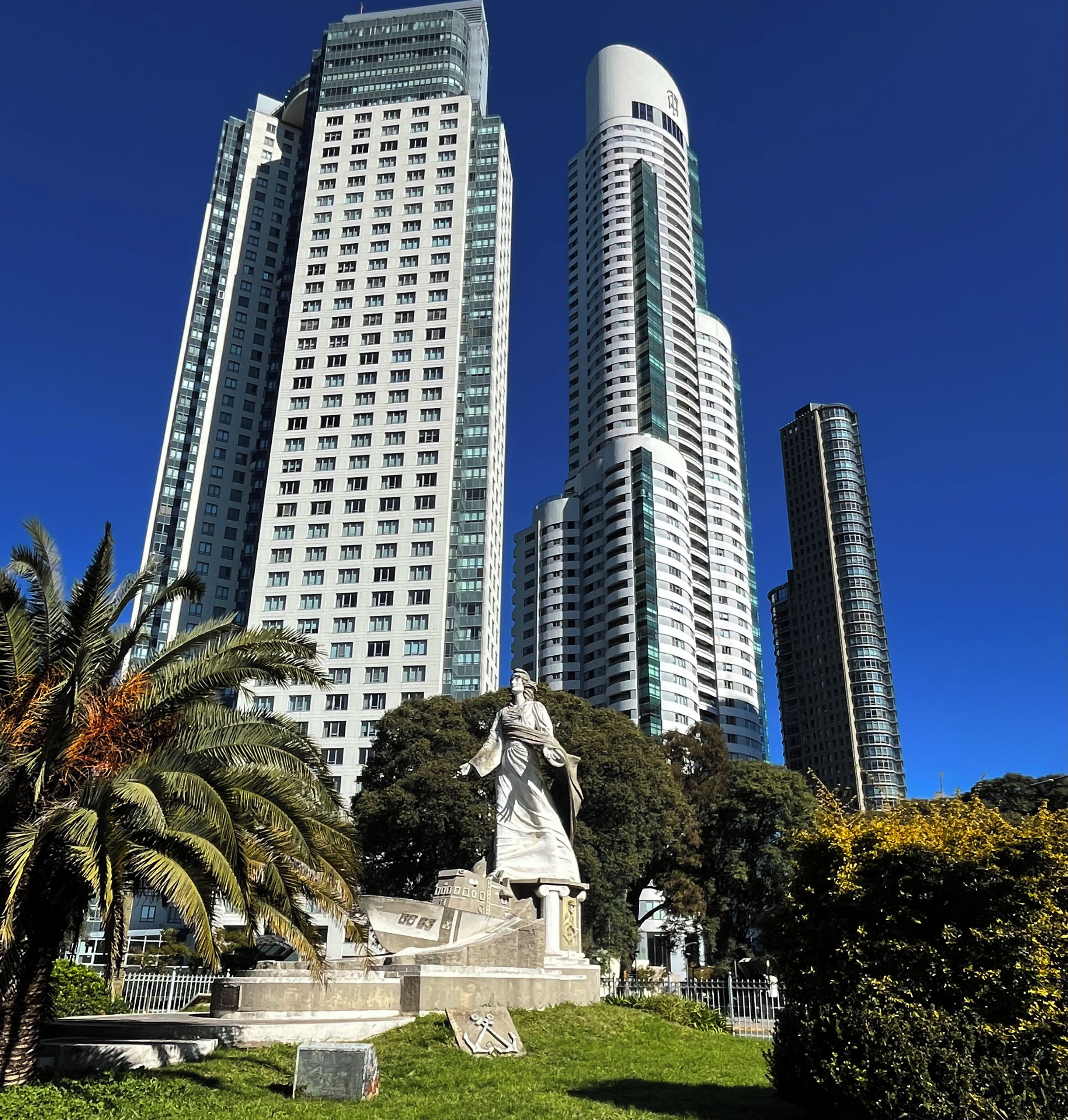 Una estatua en un parque con palmeras y un cielo azul despejado.