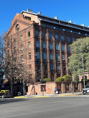 A multi-story brick building with a flat roof, large windows, and a visible street corner. - Moderno Monoambiente a pasos Obelisco (Buenos Aires)