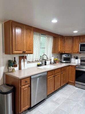 Una cocina con armarios de madera, lavavajillas de acero inoxidable, microondas y estufa.