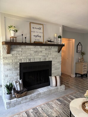 A fireplace with a brick design, a mantel shelf with decorative items, and a motivational quote above it.