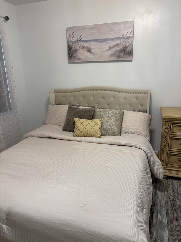 A bed with a tufted headboard, a beige quilt, and several pillows.