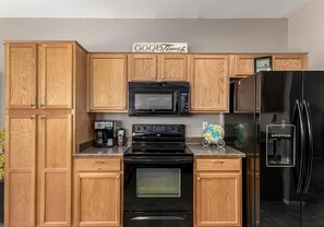 A kitchen with wooden cabinets, a black microwave, a stove, a refrigerator, and a coffee maker.