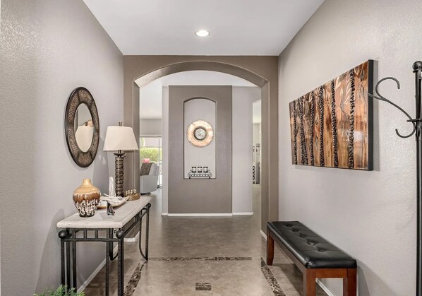 A hallway with a bench, a table with a lamp, a mirror, and a decorative wall piece.