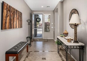 Un corridoio con una panca, un elemento decorativo a parete, una porta con vista e un tavolo con una lampada e oggetti decorativi.