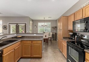 A modern kitchen with wooden cabinets, a black stove, and a dining area with a table and chairs.