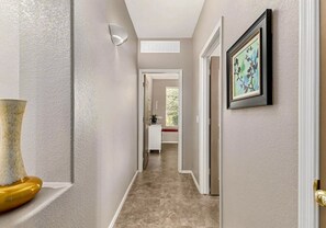 A hallway with a white door, a framed picture on the wall, and a vase on a shelf.