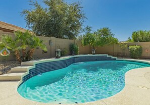 Una piscina dalla forma sinuosa, circondata da un muro color beige e diverse piante.