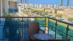 A balcony with two wicker chairs and a small table, overlooking a cityscape with modern buildings and a clear sky. - Apartment in New Alamein
Furnished Apartment for Rent in Downtown New Alamein (Marsa Matrouh Governorate)