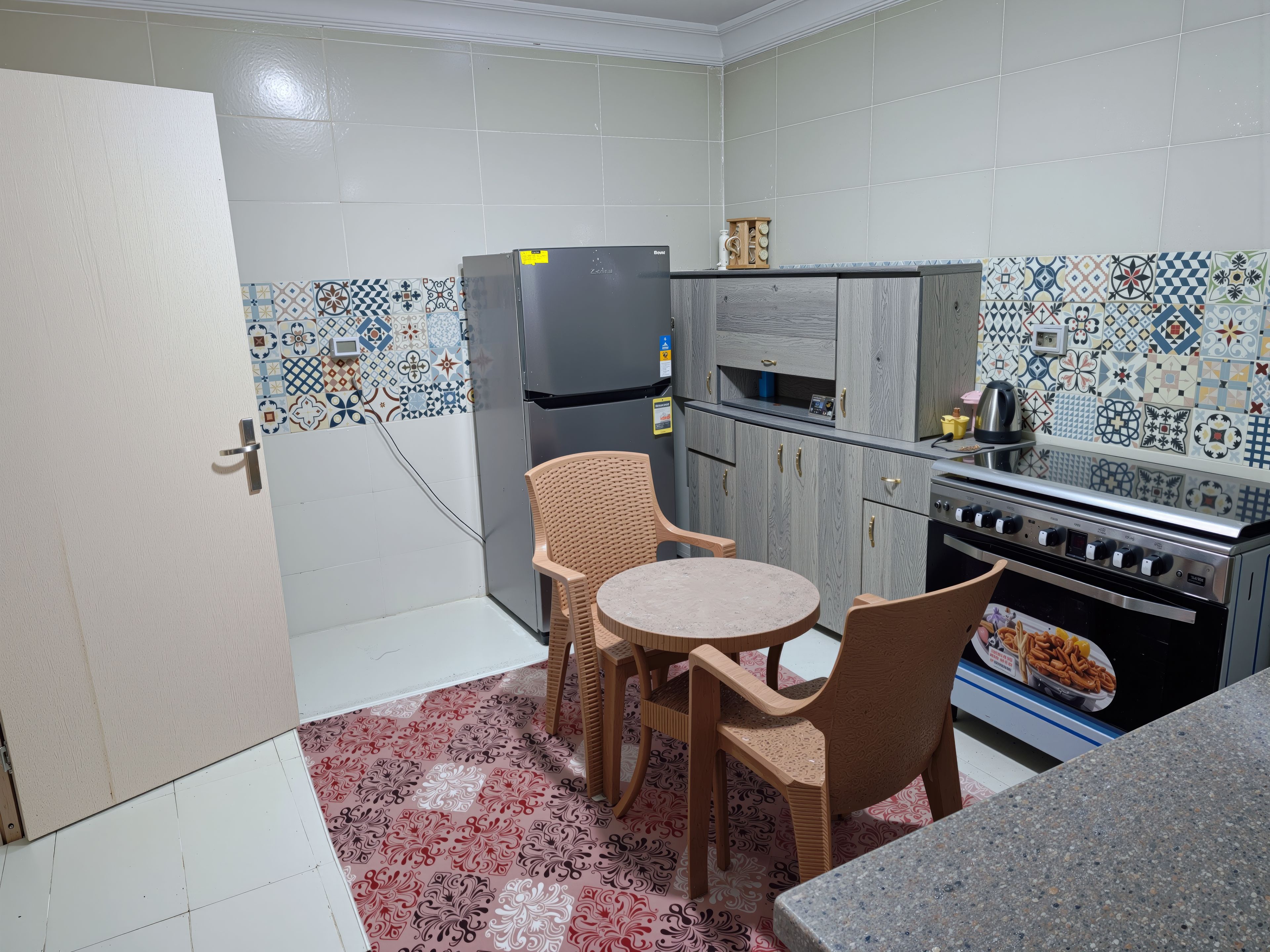 Eine kleine Küche mit Kühlschrank, Herd und einer Essecke mit zwei Stühlen.