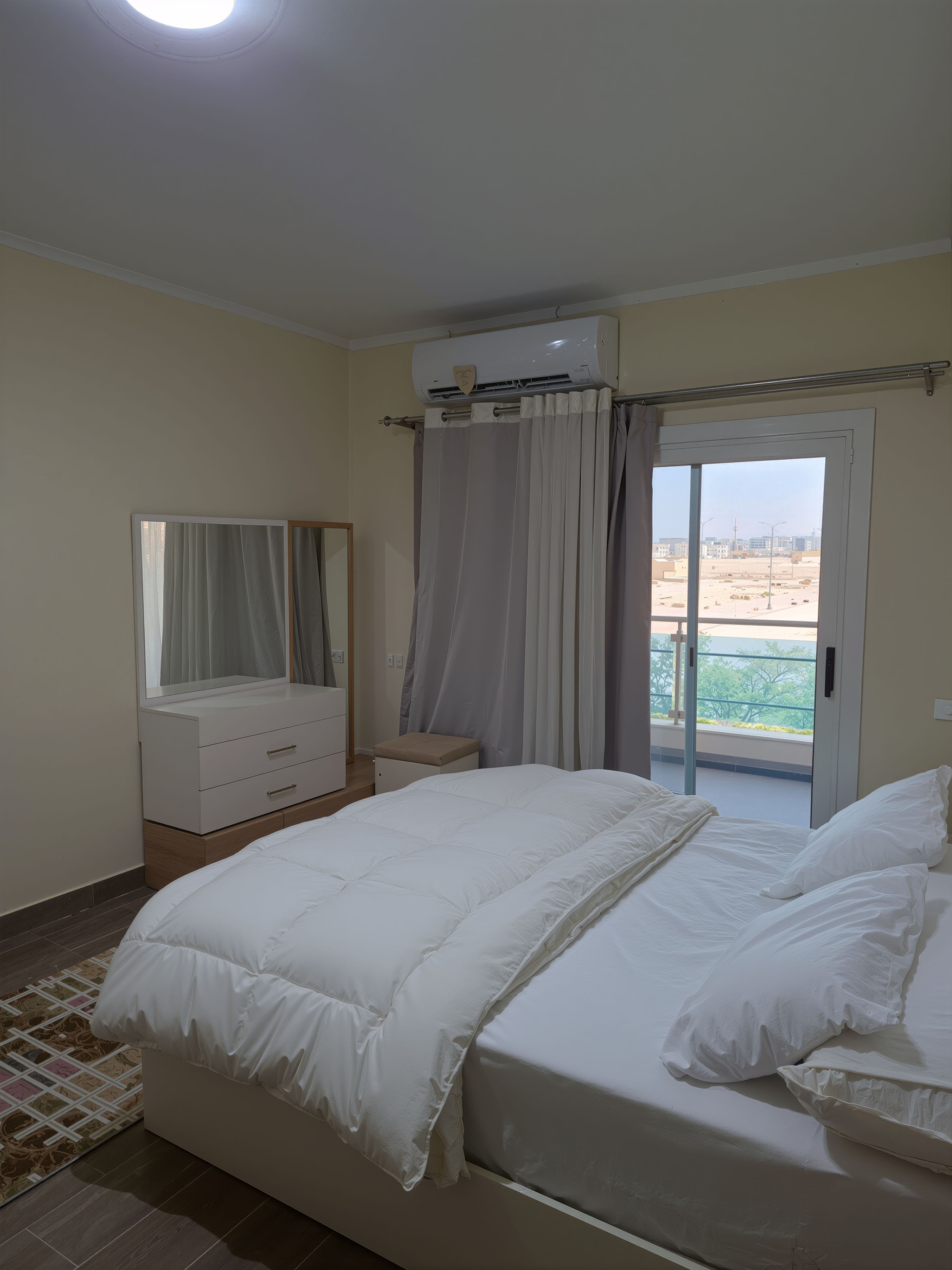 Ein Schlafzimmer mit Bett, Kommode, Spiegel und einer Glastür, die auf einen Balkon führt.