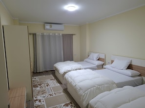 Hotellihuone, jossa on kaksi erillistä sänkyä, vaatekaappi, kattoon asennettu ilmastointilaite ja kuviollinen matto.