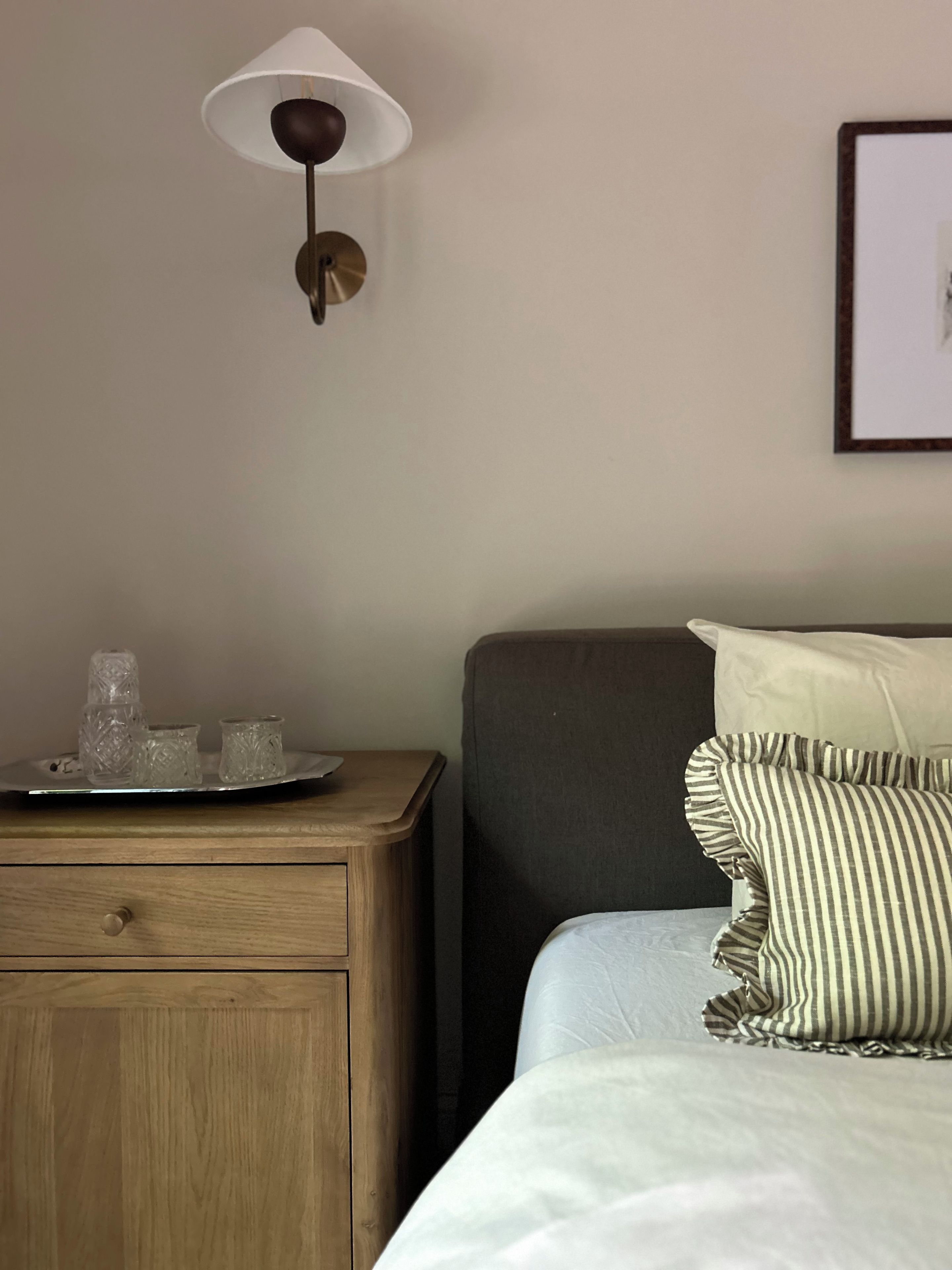 A neatly arranged hotel room with a bed, bedside table, lamp, and a framed picture on the wall.