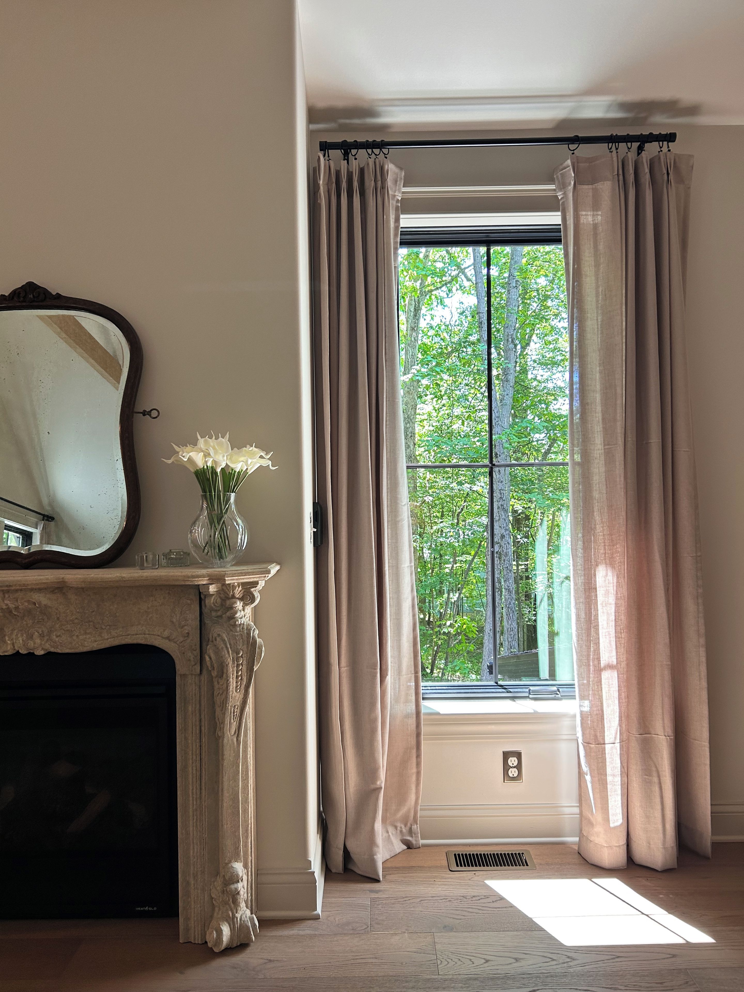 Une pièce avec une cheminée, un miroir et une fenêtre avec des rideaux.