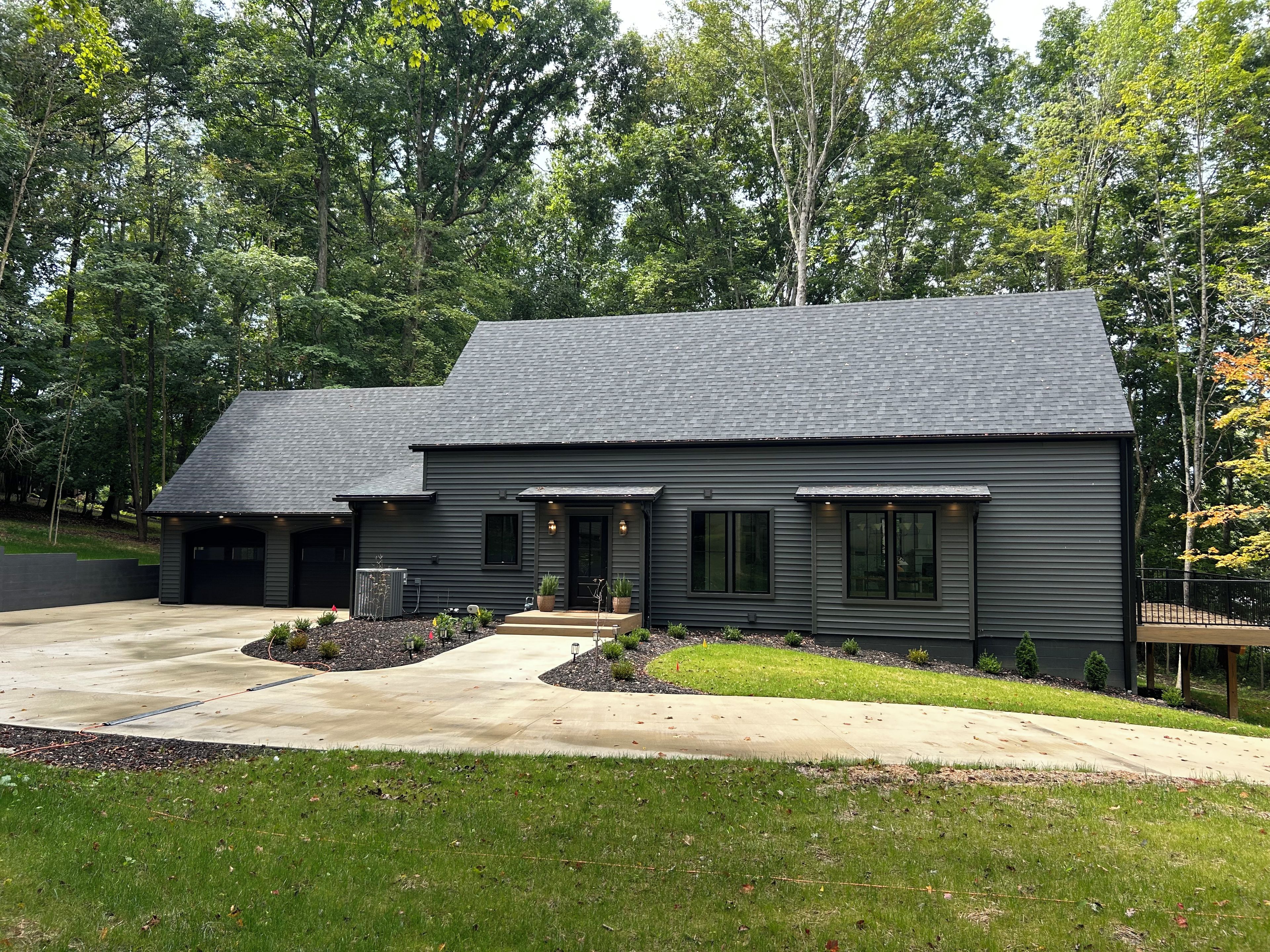 A modern two-story house with a dark exterior, a driveway, and a well-maintained lawn.
