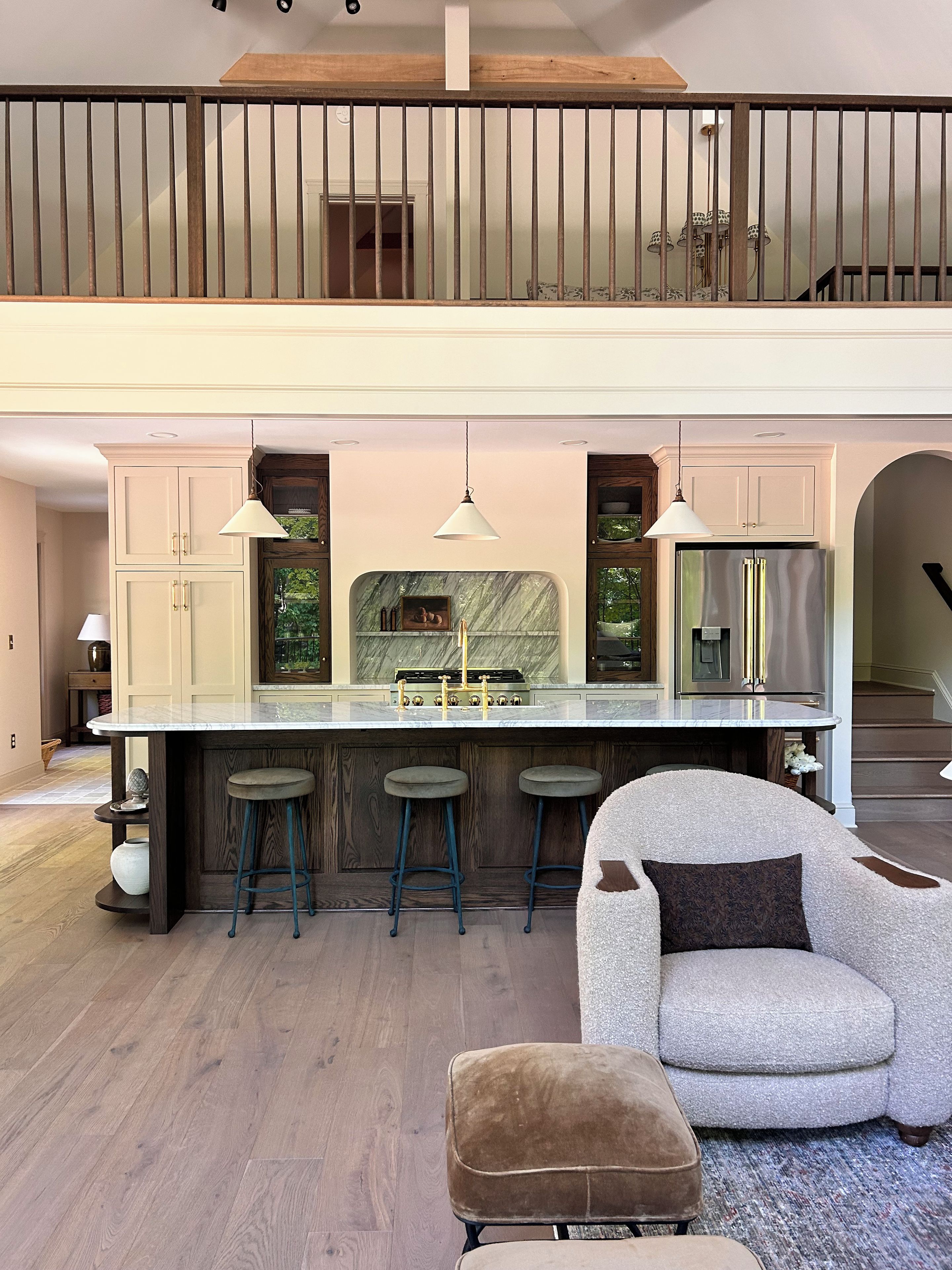 A spacious kitchen with a high ceiling, a central island with stools, and a view of a balcony.