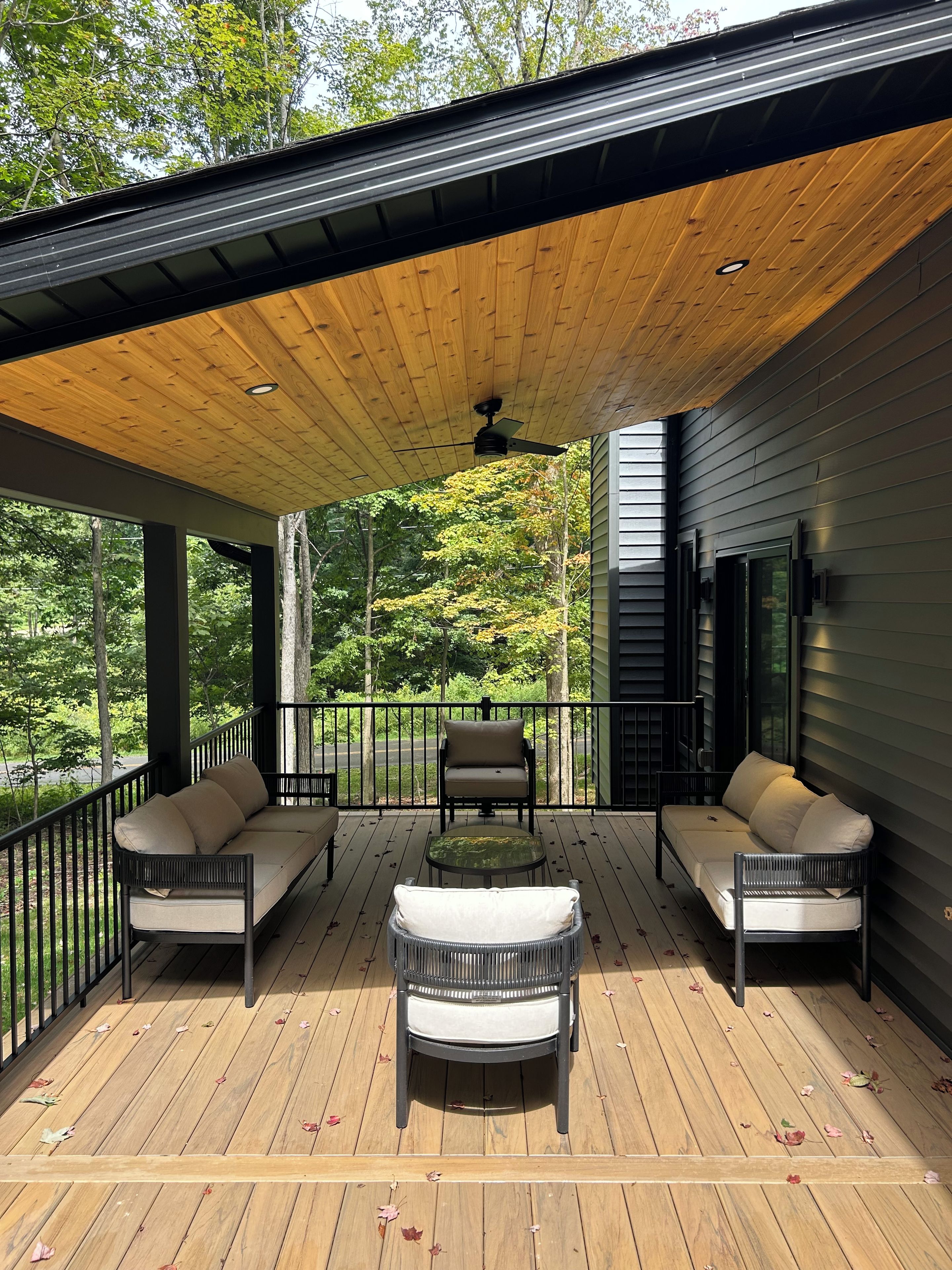 A covered deck with a ceiling fan, two sofas, a small table, and a chair.