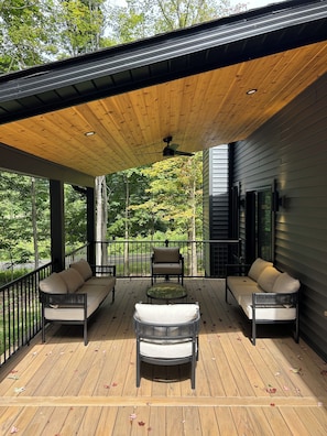 A covered deck with a ceiling fan, two sofas, a small table, and a chair.