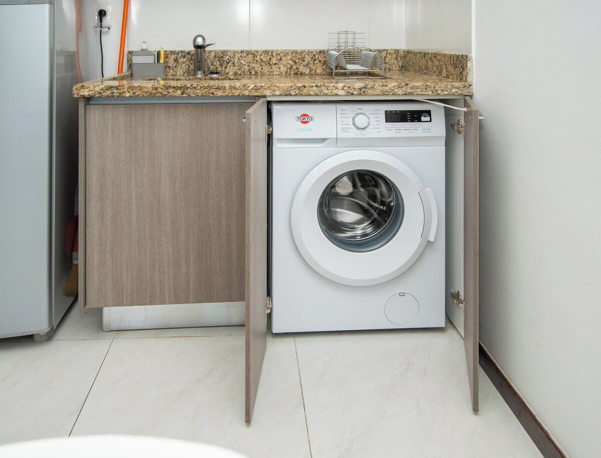 Una lavadora compacta en una cocina moderna con un mueble de madera y una encimera de granito.