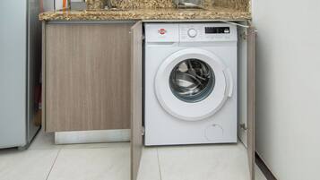 Una lavadora compacta en una cocina moderna con un mueble de madera y una encimera de granito.