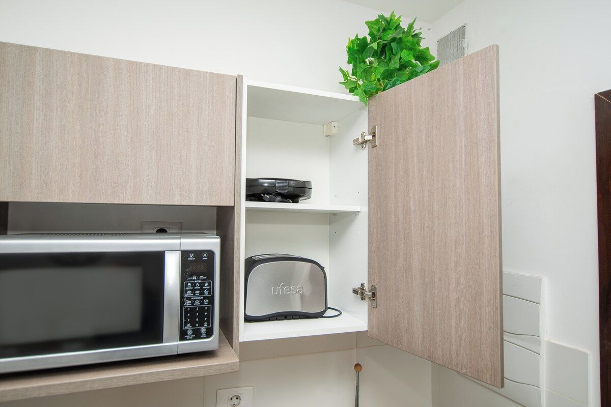 A kitchen with a microwave, toaster, and a cabinet with a plant on top.