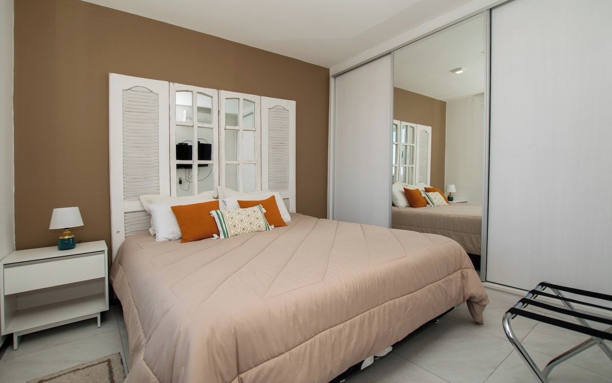 A bedroom with a large bed, white nightstands, a lamp, and a sliding door closet.
