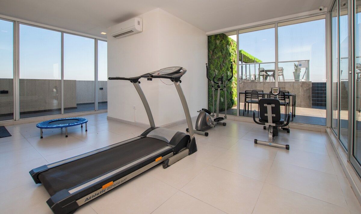 A modern gym with a treadmill, elliptical, and weights, large windows, and a view of the outdoors.
