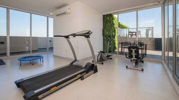 A modern gym with a treadmill, elliptical, and weights, large windows, and a view of the outdoors.