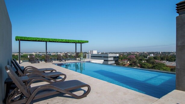 A rooftop pool area with lounge chairs, a pergola with greenery, and a city view. - Fully Equipped Apt, Pool & Workspace, City Views (Asunción)