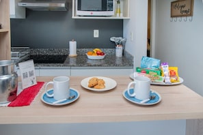 En frukostuppsättning med två vita koppar på fat, en tallrik med kakor och olika frukosttillbehör på bänken.