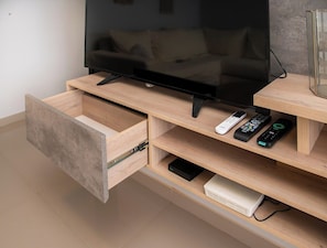 Un meuble de divertissement moderne doté d’un téléviseur à écran plat, de télécommandes et d’un tiroir.