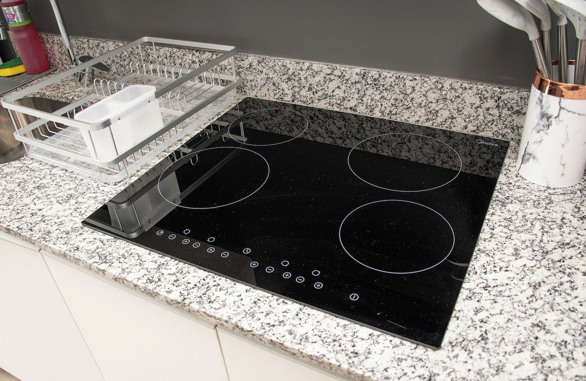 Una cocina con tope de inducción negro, escurreplatos y encimera de mármol.