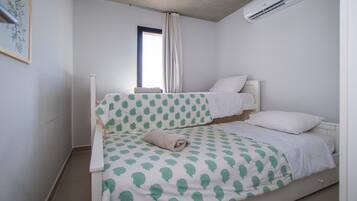 Un lit simple avec une couvre-lit à motifs, une fenêtre avec des rideaux et un appareil de climatisation fixé au mur.