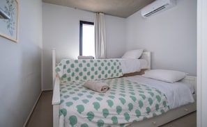 Un lit simple avec une couvre-lit à motifs, une fenêtre avec des rideaux et un appareil de climatisation fixé au mur.