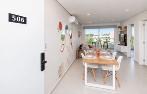 A modern dining area with a wooden table set for four, white chairs, and a view of the cityscape through large windows. - Urban Oasis with Pool, BBQ and Nearby Shopping (Asunción)
