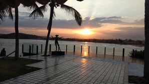A sunset view from a waterfront promenade with a tiled walkway, palm trees, and a statue. - Cinematic mansion Geriba and Ferradurinha (Armação dos Búzios)