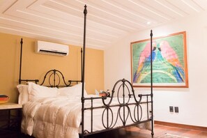 A four-poster bed with a white comforter, a wall-mounted air conditioner, and a colorful painting of parrots. - Cinematic mansion Geriba and Ferradurinha (Armação dos Búzios)