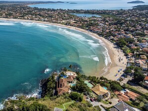 An aerial view of a coastal town with a beach, houses, and a small resort area with a pool. - Cinematic mansion Geriba and Ferradurinha (Armação dos Búzios)