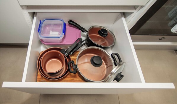 A kitchen drawer containing various cookware items including pots, pans, and a plastic container.
