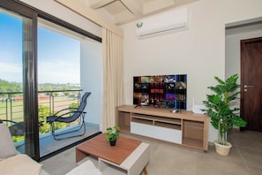 Sala de estar moderna com uma televisão grande, uma varanda com cadeira e uma planta em vaso.