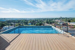 Una piscina en la terrassa amb un solàrium de fusta, envoltada d'una barana de metall, amb vista a un paisatge urbà.