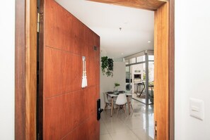 A modern interior with a wooden door, a dining area with a table and chairs, and a visible plant. - Modern Retreat with Pool, Gym and Private Balcony (Asunción)